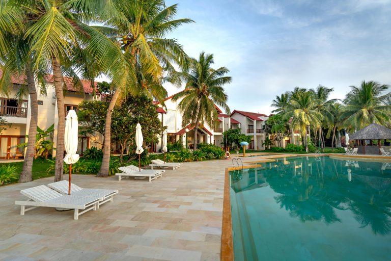 Relaxing poolside view with coconut trees and villas at a tropical resort.