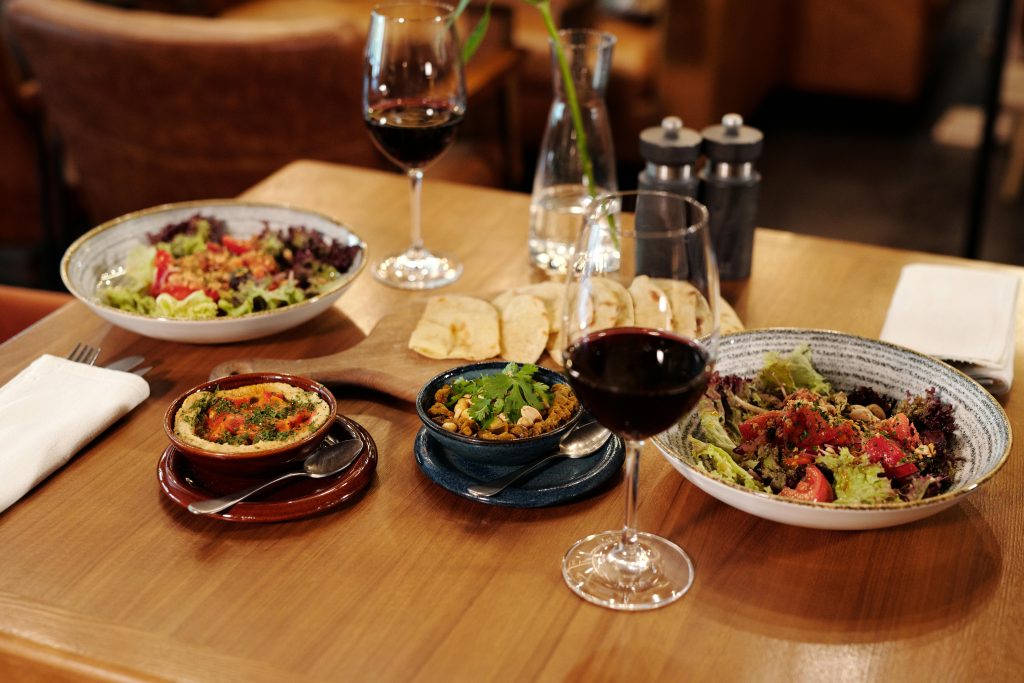 A beautifully arranged table featuring plates of Mediterranean food and glasses of red wine, set in a cozy restaurant atmosphere.
