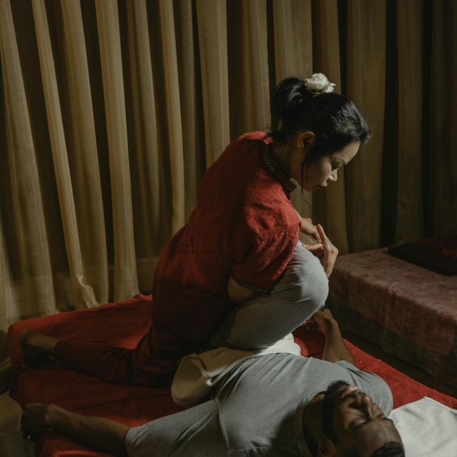 A therapist performs a massage in a dimly lit room, ensuring client relaxation and care.