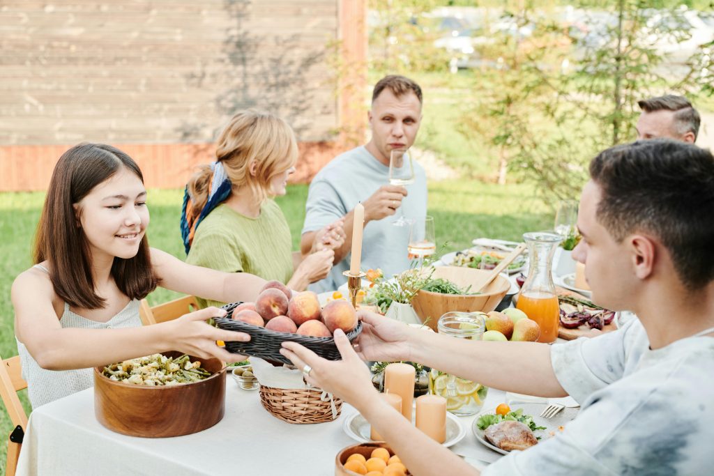 Family gathering for an outdoor lunch with fruits and salads, promoting togetherness and healthy eating.