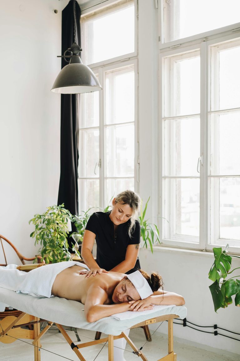 A soothing massage in a well-lit spa room with plants and natural light.